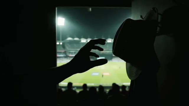 Silhouette of a Cricketer Reaching for Helmet Before Night Match