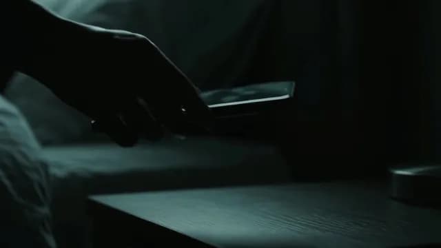 Hand Reaching for Smartphone on Nightstand in Dimly Lit Room