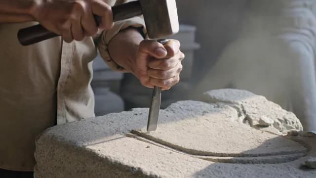 Skilled Artisan Carving Stone with Hammer and Chisel in Workshop