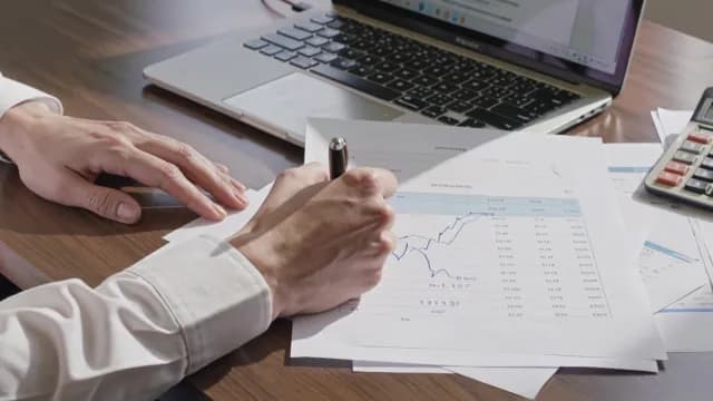Close-up of hands analyzing financial charts and writing on documents
