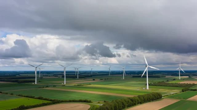 Aerial View of Wind Turbines in Green Agricultural Fields Under Cloudy Sky