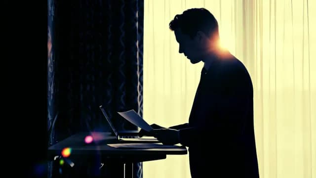 Silhouette of Businessman Working on Laptop and Reviewing Documents in Office