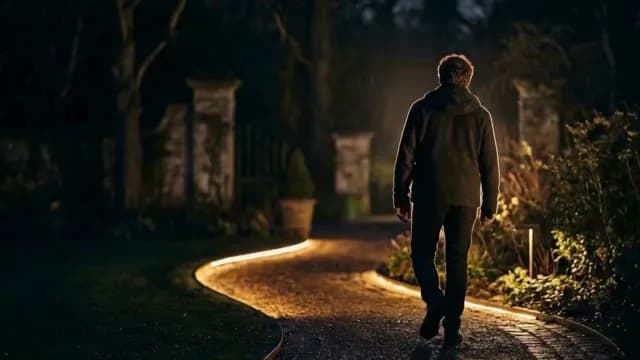 Man Walking Down Illuminated Garden Path at Night