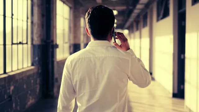 Businessman Walking Down Industrial Hallway Talking on Smartphone