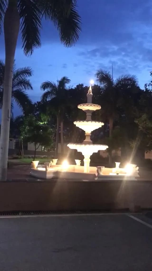 Illuminated Three-Tiered Garden Fountain Glowing at Dusk Under Palm Trees