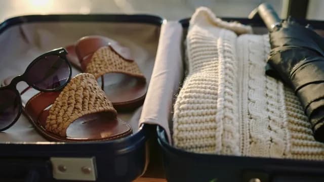 Travel Packing Concept with Summer Sandals and Winter Sweater in Suitcase