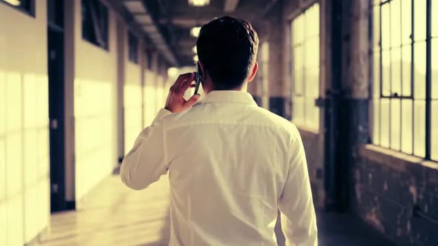 Businessman Walking Down Industrial Hallway Talking on Mobile Phone