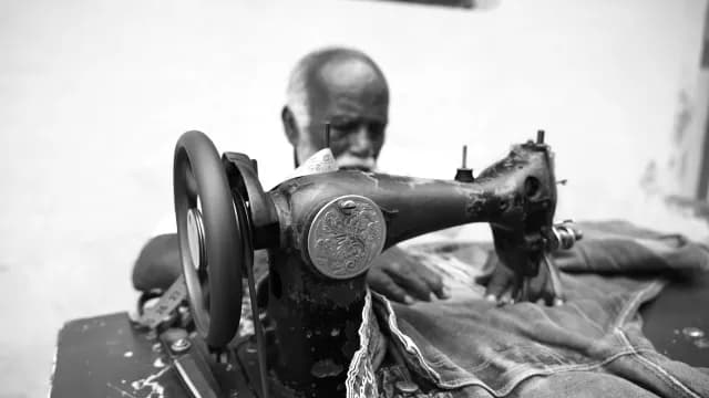 Elderly Tailor Working on Vintage Sewing Machine in Black and White